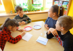 Czwórka dzieci czyta nazwy produktów spożywczych zapisanych na karteczkach.